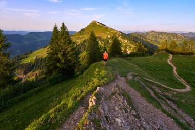 pretty senior woman hiking in warm dawn sunlight and enjoying the spectacular view over the Allgau alps on the Nagelfluh mountain chain near Oberstaufen, Bavaria, Germany