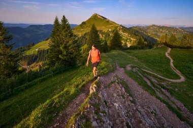pretty senior woman hiking in warm dawn sunlight and enjoying the spectacular view over the Allgau alps on the Nagelfluh mountain chain near Oberstaufen, Bavaria, Germany