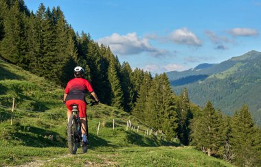 pretty senior woman riding her electric mountain at sunset in the Allgau alps below the Nagelfluh mountain chain next to Steibis, Bavaria, Germany 