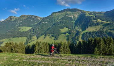 pretty senior woman riding her electric mountain at sunset in the Allgau alps below the Nagelfluh mountain chain next to Steibis, Bavaria, Germany 