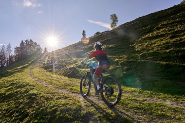 pretty senior woman riding her electric mountain at sunset in the Allgau alps below the Nagelfluh mountain chain next to Steibis, Bavaria, Germany 