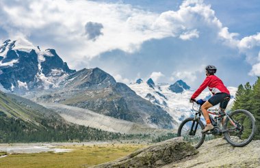 Sella Grubu 'nun buzulları ve Piz Roseg, Engadin, İsviçre' nin zirvelerinin altındaki Roseg vadisinde e-dağ bisikleti süren aktif yaşlı bir kadın.