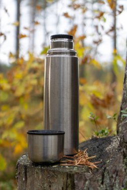 Ormanda bir kütüğün üzerinde termos. Arka planda, sonbahar güneşiyle çevrili bulanık ormanı görebilirsiniz..