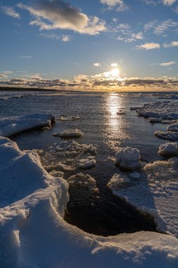 Mavi gökyüzü ve nehir suyunun denize aktığı Lilaste sahilindeki küçük bulutlarla birlikte gün batımı buz ve kar arasında yol alır..