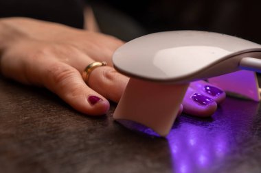 Elinde birkaç parmağı olan küçük bir ultraviyole lamba. Evdeki mor ışık, yeni uygulanmış jöle ojesiyle tırnakları aydınlatıyor..