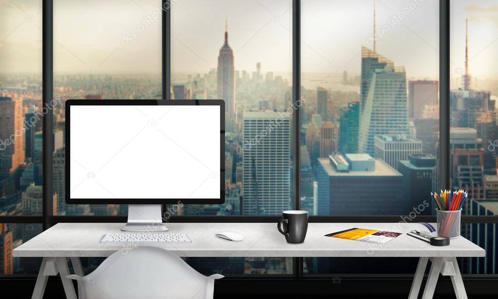 Isolated computer display for mockup in office interior overlooking the city and skyscrapers. Work desk with keyboard, mouse, cup of coffee, paper, pencils.