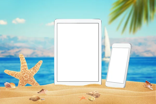 White tablet and smart phone with isolated white screen for mockup. Summer on beach, sea, sand, blue sky, palm, starfish and shells.