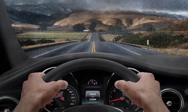 Conduciendo con tiempo lluvioso. Vista desde el ángulo del conductor mientras las manos en el volante. Lluvia salpicada parabrisas —  Fotos de Stock