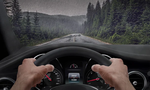 Rijden in de regen. Uitzicht vanaf de hoek van de bestuurder terwijl de handen op het wiel. Regen gevlekte voorruit — Stockfoto