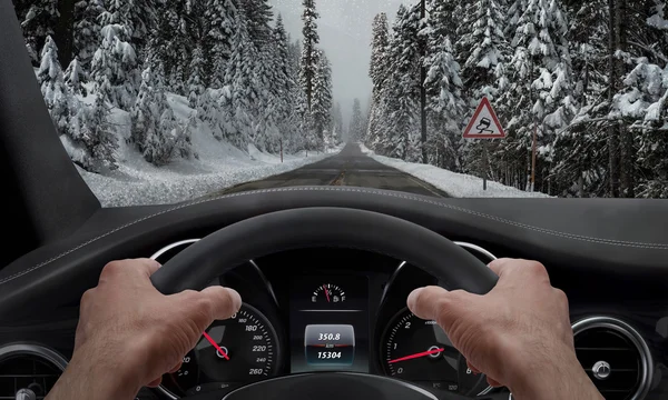 Rijden in het besneeuwde weer. Uitzicht vanaf de hoek van de bestuurder terwijl de handen op het wiel. Naast de weg is een teken voor gladde weg. — Stockfoto