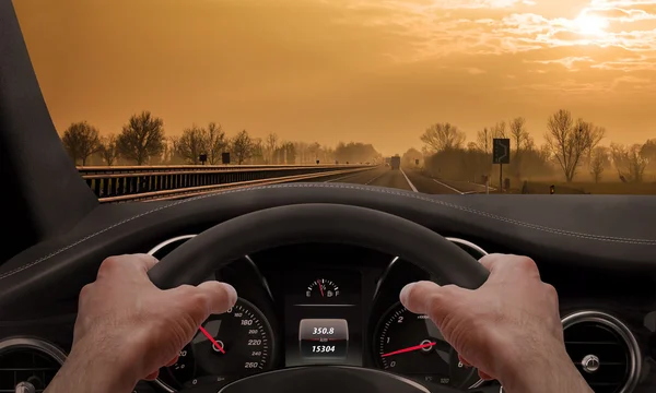 Rijden bij zonsondergang. Uitzicht vanaf de hoek van de bestuurder terwijl de handen op het wiel. — Stockfoto