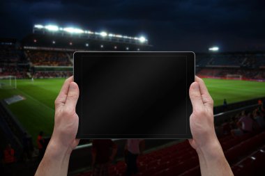 Adam futbol oyunu boş ekran ile tablet tutan. Arka planda stadyum. 