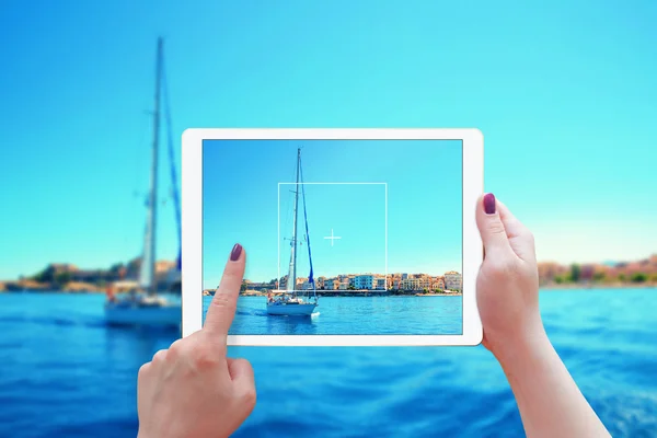 Frau fotografiert Jacht und Stadt mit Tablet. Frau hält weiße Tablette in der Hand. — Stockfoto