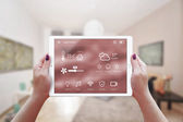 Smart Remote Home Control App in der Hand einer Frau. Wohnzimmerausstattung im Hintergrund.