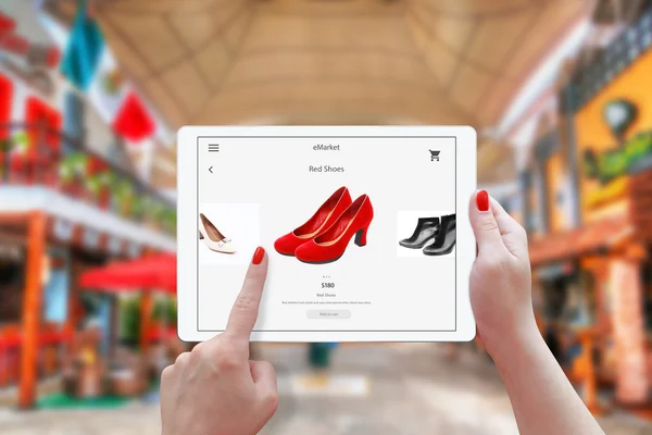 여자 온라인의 태블릿 쇼핑입니다. 장치를 개최 하 고 빨간 구두를 선택. 백그라운드에서 쇼핑 센터. — 스톡 사진