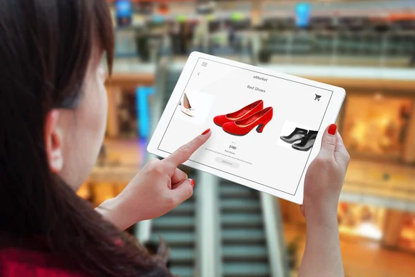 Donna shopping online con tablet. Tenere dispositivo e scegliere scarpe rosse. Centro commerciale sullo sfondo . — Foto Stock