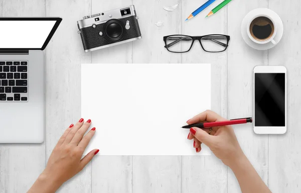 Designer schreibt auf ein leeres Papier. Draufsicht auf den Schreibtisch mit Computer, Telefon, Kamera, Brille, Kaffee. — Stockfoto