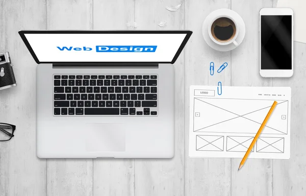 コンピューターと紙の上の web サイトのアイデア。コンピューター、携帯電話、カメラ、メガネ、コーヒー付きの仕事机の上から見る. — ストック写真