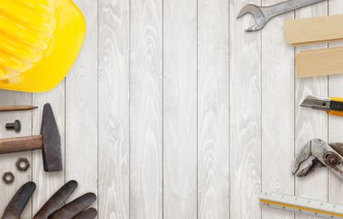 Ahşap masa üstünde inşaat işçisi alet. Kask, çekiç, eldiven, kalem pense, neşter yanında.