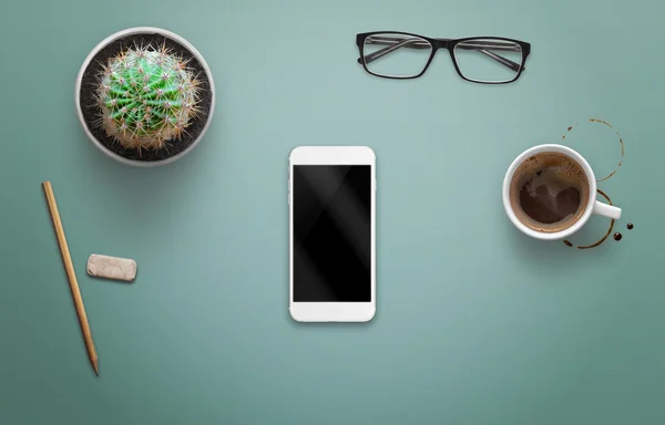 Ahşap masa boş ekran ile akıllı telefon. Yanında kahve, bitki, gözlük.