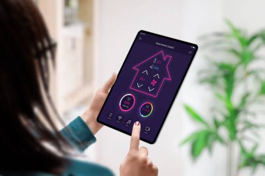 Kadın ellerinde tablet üzerindeki akıllı ev kontrol uygulaması konsepti. Arka planda ev içi