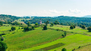 Drone view of small Orthodox church surrounded by fields and hills