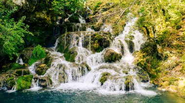 Cascading water over mossy stones surrounded by green vegetation