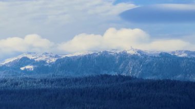 Parlak ışık, karla kaplı yüksek dağ zirvelerini, ormanlık tepelerin ve açık gökyüzünün üzerinde durduğunu gözler önüne seriyor.