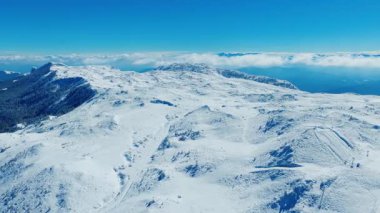 Derin mavi kış göğü altında parlak karlı dağ sırtları ve vadilerinden oluşan hava manzarası.