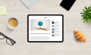 Tablet, modern dijital iletişimi ve yaşam tarzını temsil eden, kahve, kruvasan ve gözlüklerle ahşap masa üzerinde haber makalesi sergiliyor.