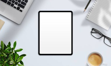 Boş ekranlı tabletin üst görünümü, kahve, not defteri, dizüstü bilgisayar ve bitki modern ışık masasında dijital tasarım için hazır.