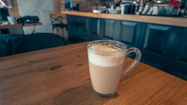 Şehir kafesinin penceresinin yanındaki ahşap masada cam bir fincan kahve, sabah ışığı yaşam tarzı ve iş kavramları için mükemmel sıcak bir atmosfer yaratıyor.