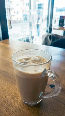 Cam bardakta köpüklü kahvenin dikey görüntüsü rahat kafenin içindeki ahşap masada, yaşam tarzı, konukseverlik ve yemek fotoğrafçılığı için mükemmel.