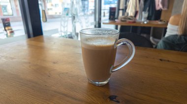 Kafenin içindeki parlak pencerenin yanındaki ahşap masanın üzerinde sıcak kahve. Yaşam tarzı ve rahatlama kavramları için modern atmosfer ideal..