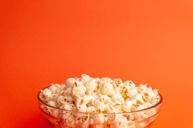 Turuncu arka planda cam bir kasede patlamış mısırın yakın çekimi, ticari ve yaratıcı kullanım için ideal doku, detay ve gıda konseptini gösteriyor