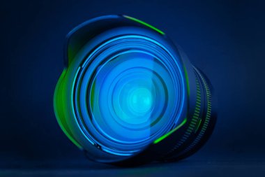 Profesyonel kamera merceğinin ön görüntüsü koyu arkaplanda mavi ve yeşil ışıkla parlıyor