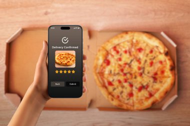 Açık kutunun üzerindeki pizza siparişini onaylayan teslimat uygulaması ile el ele tutuşan akıllı telefon, çevrimiçi yemek servisi ve hızlı teslimat kavramı