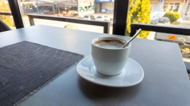 Modern kafe masasında kaşık ile bir fincan kahve, sabah ışığı ve rahatlatıcı yaşam tarzı atmosferi