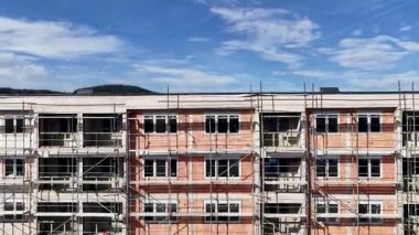 İnsansız hava aracı, inşaat halindeki modern binanın yörüngesinde, iskele ve turuncu cepheli, güneşli hava manzaralı.