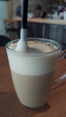 Cam fincanda saman bulunan sütlü latte kahvenin dikey videosu, yaşam tarzı veya içecek içeriği için ideal rahat kafe iç tasarımı.