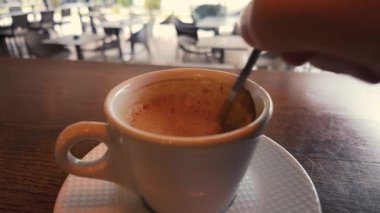 Beyaz bardakta espresso ile karıştırılmış sütlü kahve, kıvrımlı hareketler ve yumuşak dokular, rahat kafe titreşimleri.