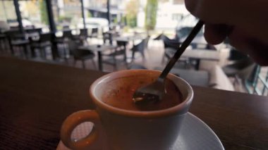 Beyaz bardakta, ahşap masada, sıcak kafeterya atmosferinde, ılık sabah yaşam tarzı konseptinde el yapımı espresso karıştırma videosu.