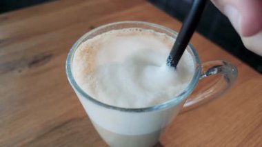 Süt köpüğünün cam kahvenin içinde yavaşça dönen makrosu, kremalı dokuya ve sıcaklığa vurgu yapıyor, içecek ve kafe marası için ideal.