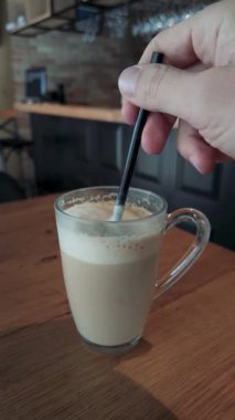 Elle karıştırılan, ahşap masada siyah pipetli kahve, pürüzsüz köpük dokusu ve sıcak renk tonlarının makro videosu.