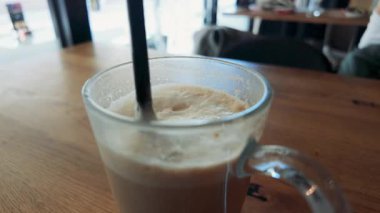 Kahve ve içecek kavramları için sıcak gün ışığında çekilmiş, cam fincanda saman bulunan latte kahvenin yatay yakın çekim videosu.