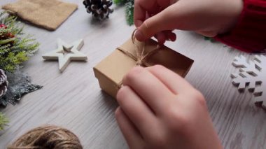 Kraft kağıdına sarılı çevre dostu bir bayram hediyesine doğal sicim bağlayan normal hızda yakın plan eller.