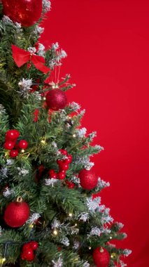 Kamera Noel ağacı kenarına doğru hareket ediyor, sağ taraftaki şenlikli dalları ve sol taraftaki temiz kırmızı kopya alanını gösteriyor.