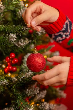 Bir Noel ağacını kırmızı bir aksesuarla süslemek, parlak kırmızı arka planda sıcak ve şenlikli bir bayram anı yaratır.