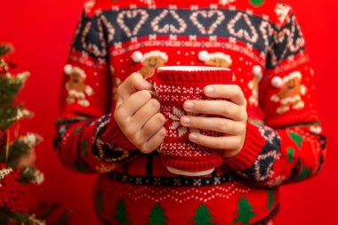 Noel süveteri giyerken elinde sıcak örülmüş bir kupa tutan çocuk, sıcak bir kış havası yaratıyor.