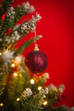 Sıcak şenlik ışıkları ve canlı bir tatil atmosferiyle süslü bir ağaca asılı parlak kırmızı bir Noel süsü.